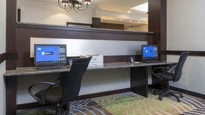 Un espacio de trabajo en un hotel con dos escritorios, cada uno con una computadora, sillas y una araña.