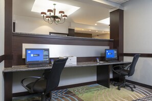 Um espaço de trabalho em hotel, com duas mesas, cada uma com um computador, cadeiras e um candelabro.