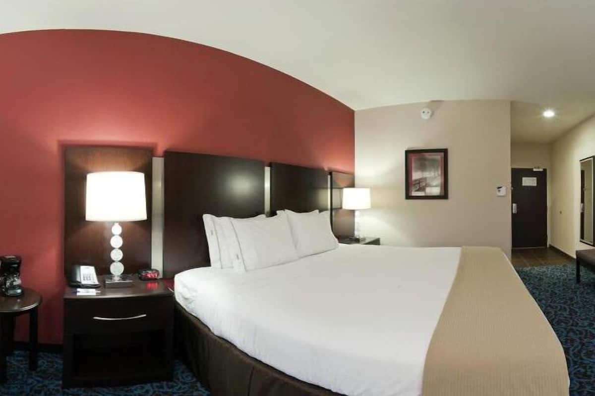 A hotel room with a large bed, two bedside tables with lamps, a desk with a chair, and a television on a stand.