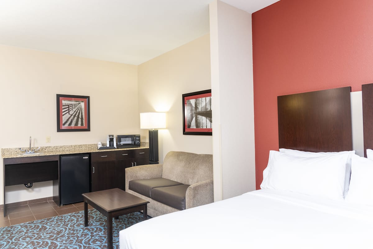 A hotel room with a bed, a desk with a computer, a refrigerator, and two framed pictures on the wall.