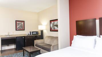 Habitación de hotel con cama, escritorio con computadora, refrigerador y dos cuadros en la pared.