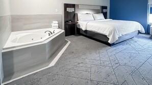 Una habitación de hotel moderna con una bañera grande, una cama con ropa de cama blanca y una pared de acento azul.