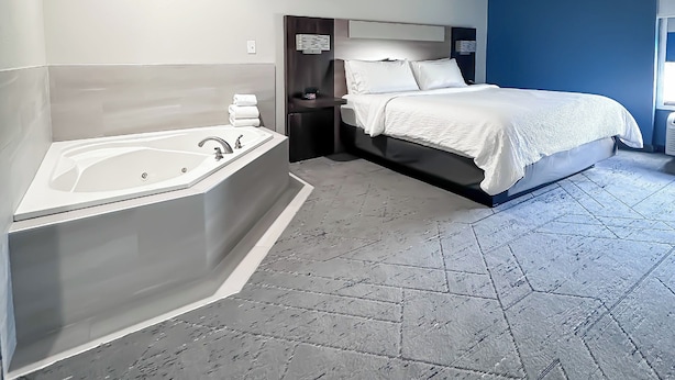A modern hotel room with a large bathtub, a bed with white linens, and a blue accent wall. - Holiday Inn Express Hotel & Suites New Philadelphia by IHG (New Philadelphia)