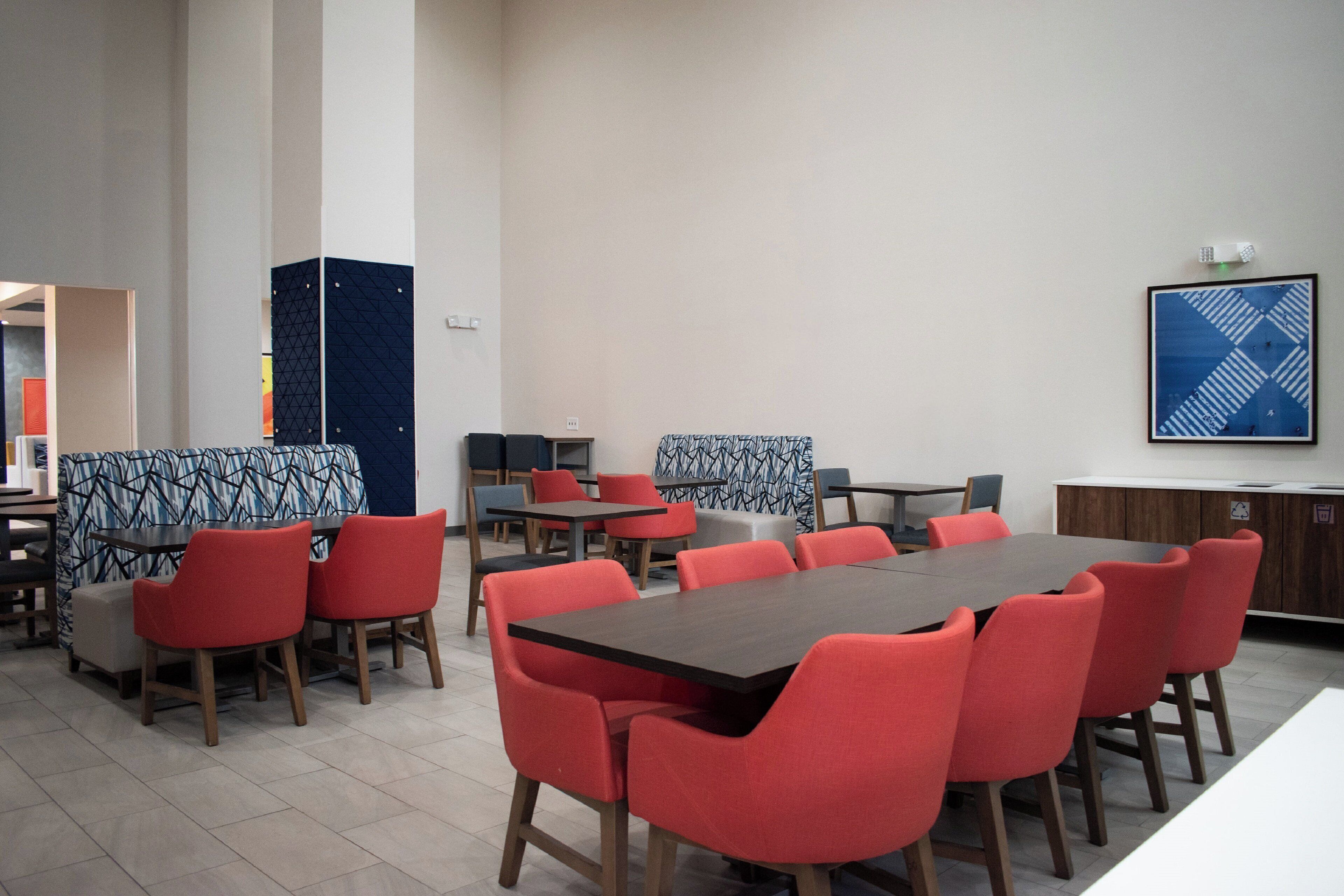 Un comedor moderno con sillas tapizadas en rojo y mesas de madera oscura. Hay cabinas con tapicería estampada y un gran cuadro abstracto en la pared.