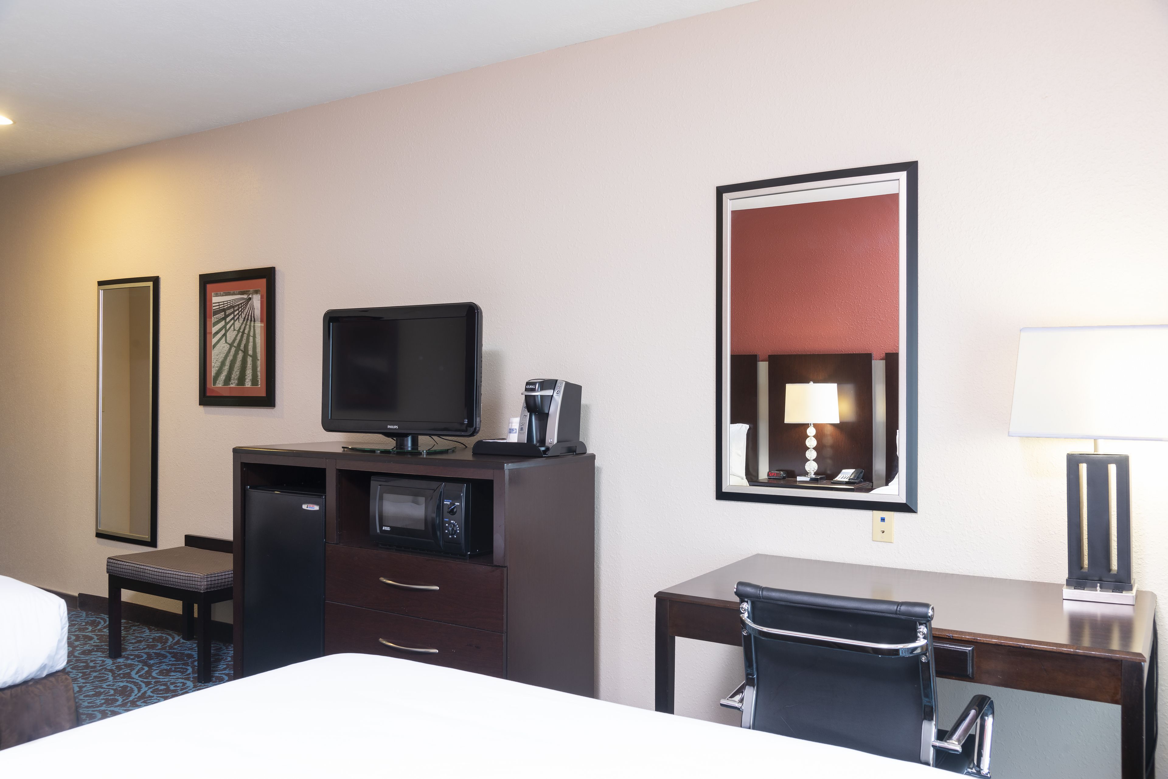 Ein Hotelzimmer mit einem Bett, einem Schreibtisch mit Stuhl, einem Fernseher, einer Kaffeemaschine, einer Mikrowelle und einem großen Spiegel.
