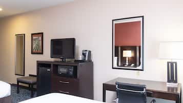 Habitación de hotel con cama, escritorio con silla, televisor, cafetera, microondas y un espejo grande.