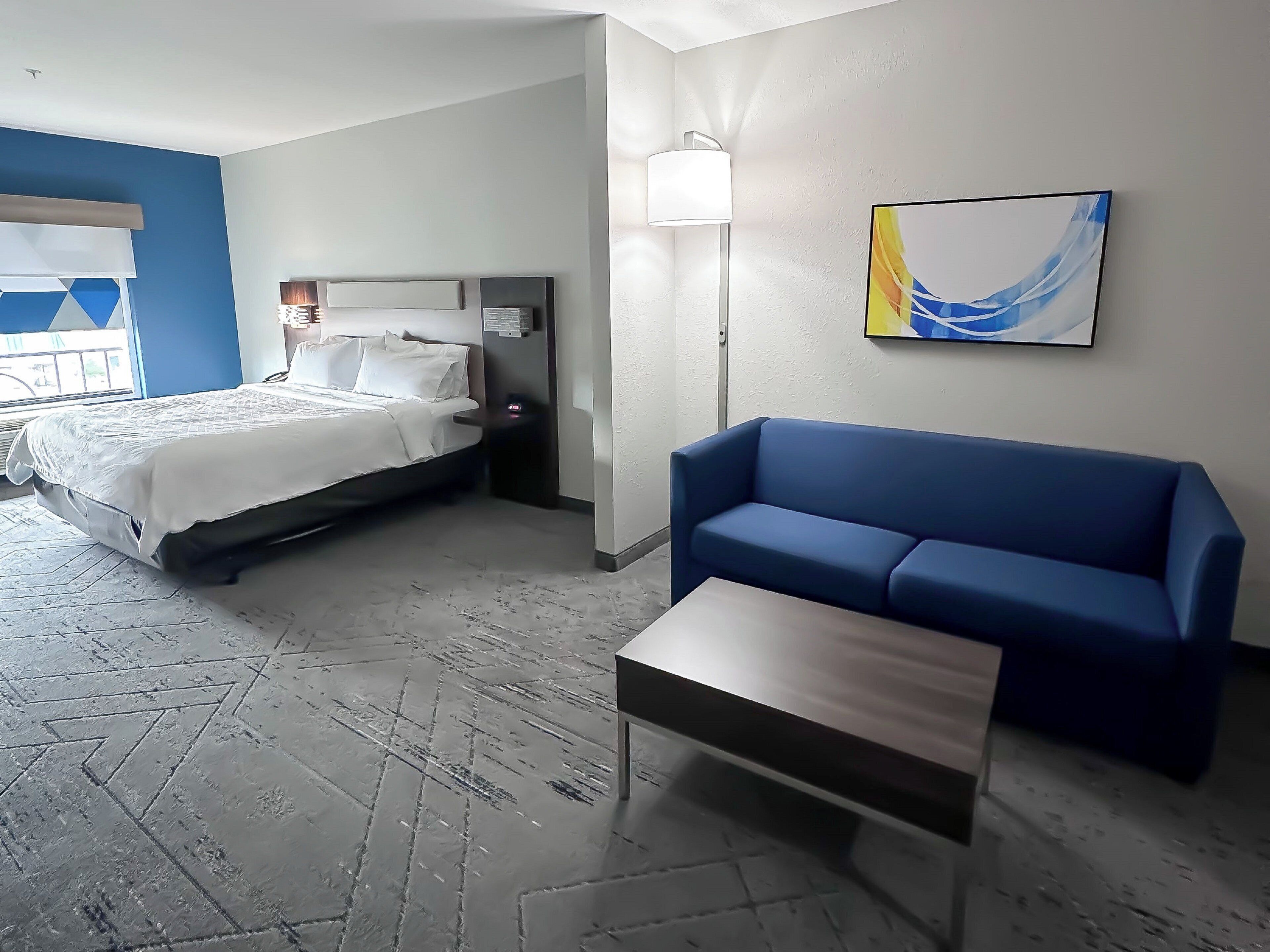 Une chambre d’hôtel avec un lit, un canapé bleu, une petite table et un tableau accroché au mur.
