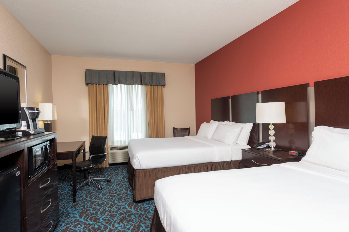 A hotel room with two beds, a desk with a computer, a chair, a TV, and a telephone.