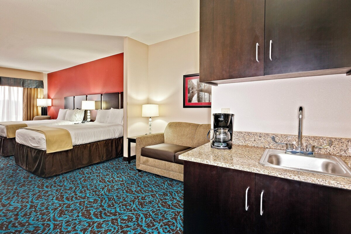A hotel room with two beds, a sofa, a coffee maker, and a sink.
