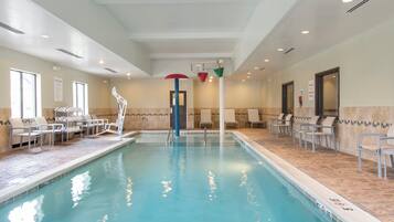 An indoor swimming pool with clear water, surrounded by lounge chairs and a tiled floor.