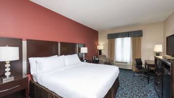 A hotel room with a large bed, a desk with a chair, a TV, and a window with curtains.