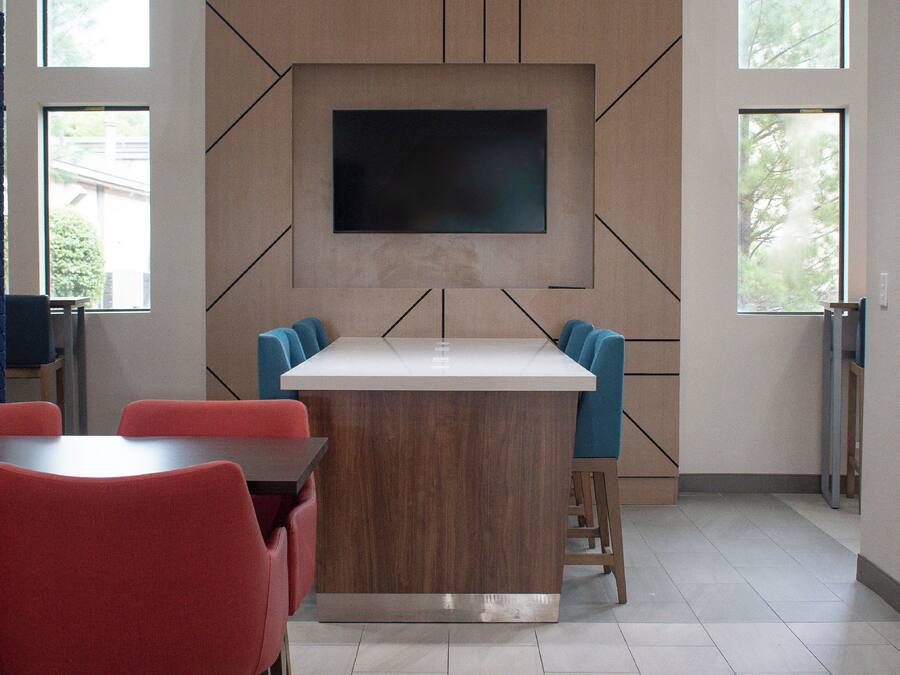 A modern interior with a central island table, red and blue chairs, and a large flat-screen TV mounted on the wall.