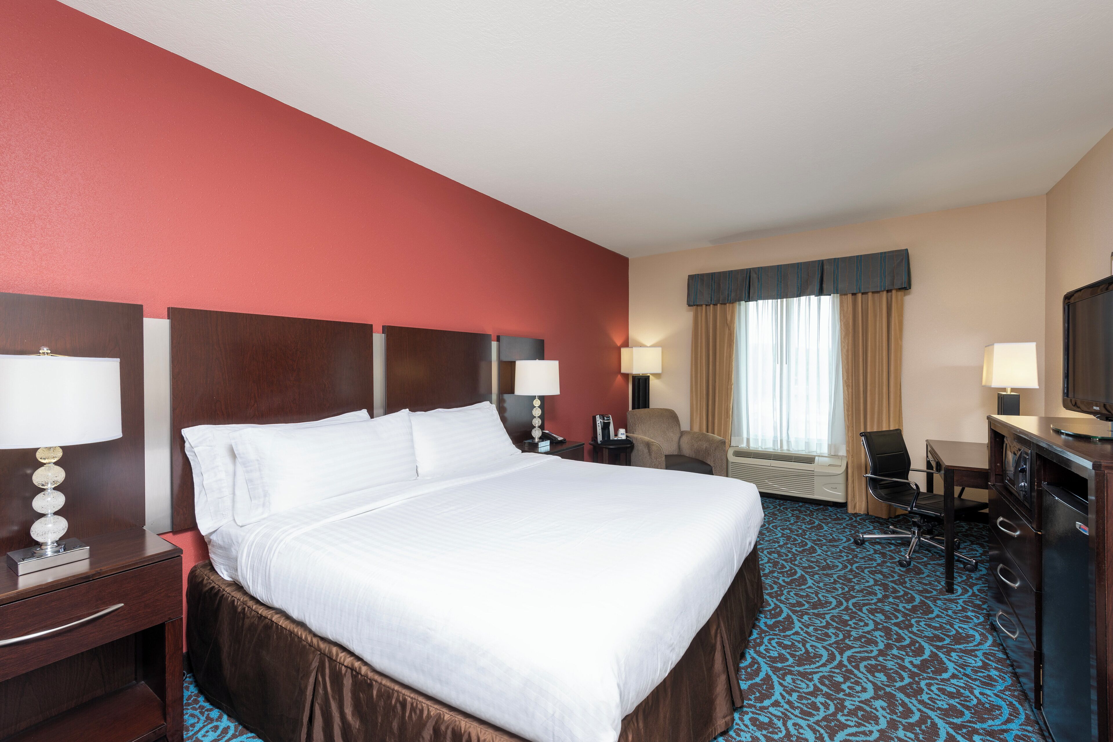 A hotel room with a large bed, a desk, a chair, a television, and a window with curtains.