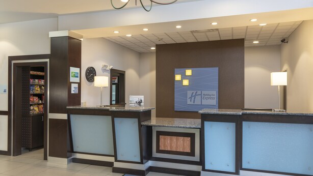 Zona de recepción de un hotel con mostrador, un reloj, el letrero de Holiday Inn Express y una máquina expendedora.