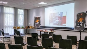 Une salle de conférence dotée d’un grand écran diffusant une présentation, de nombreuses chaises disposées en rangées et une table sur laquelle se trouvent divers objets.