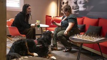 Un ambiente interior acogedor con un sofá rojo, una pequeña mesa redonda con un tablero de ajedrez y un perro acostado en el suelo.
