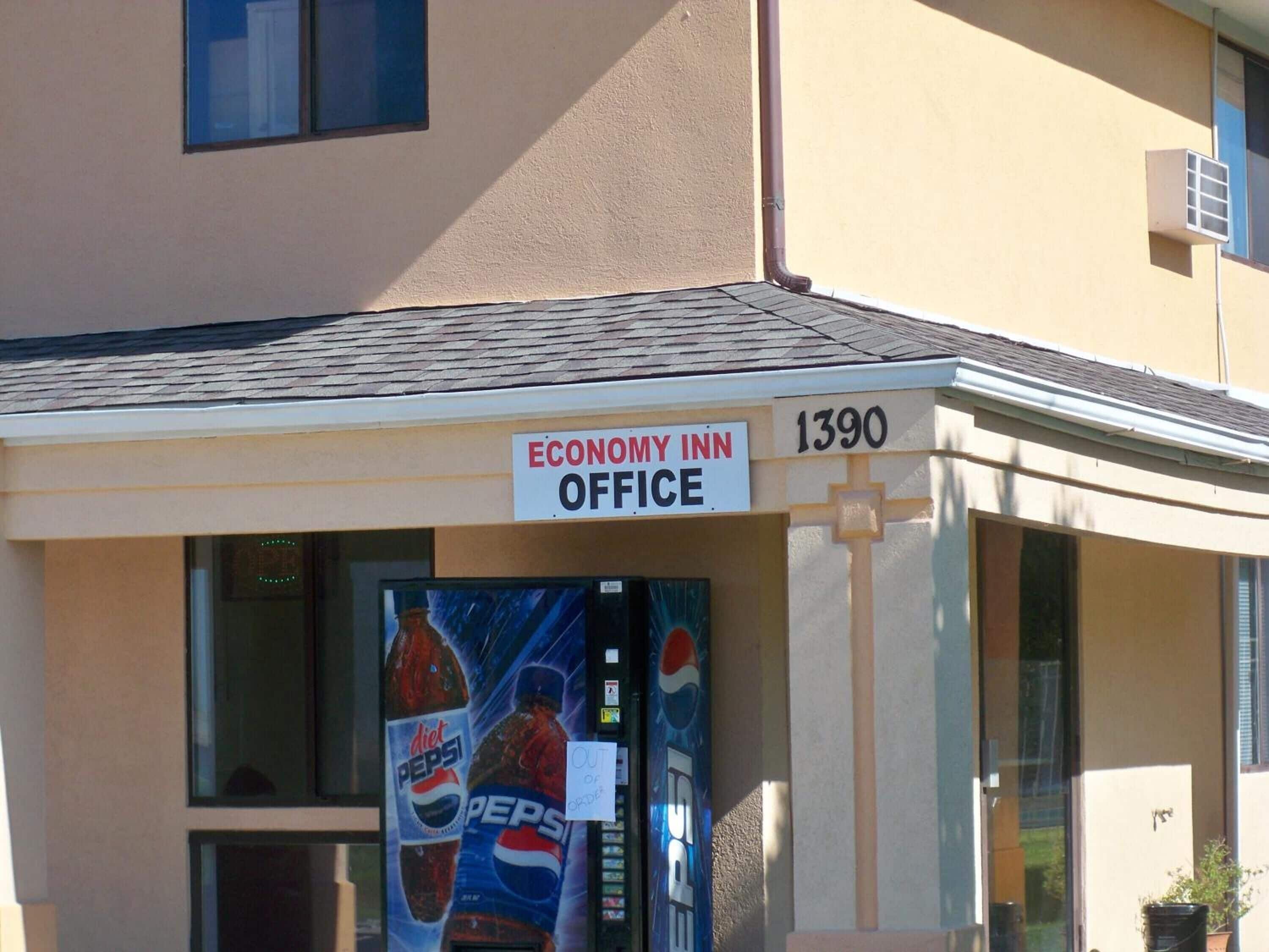 The exterior of the Economy Inn Office at 1390, featuring a Pepsi vending machine and a clear view of the entrance.