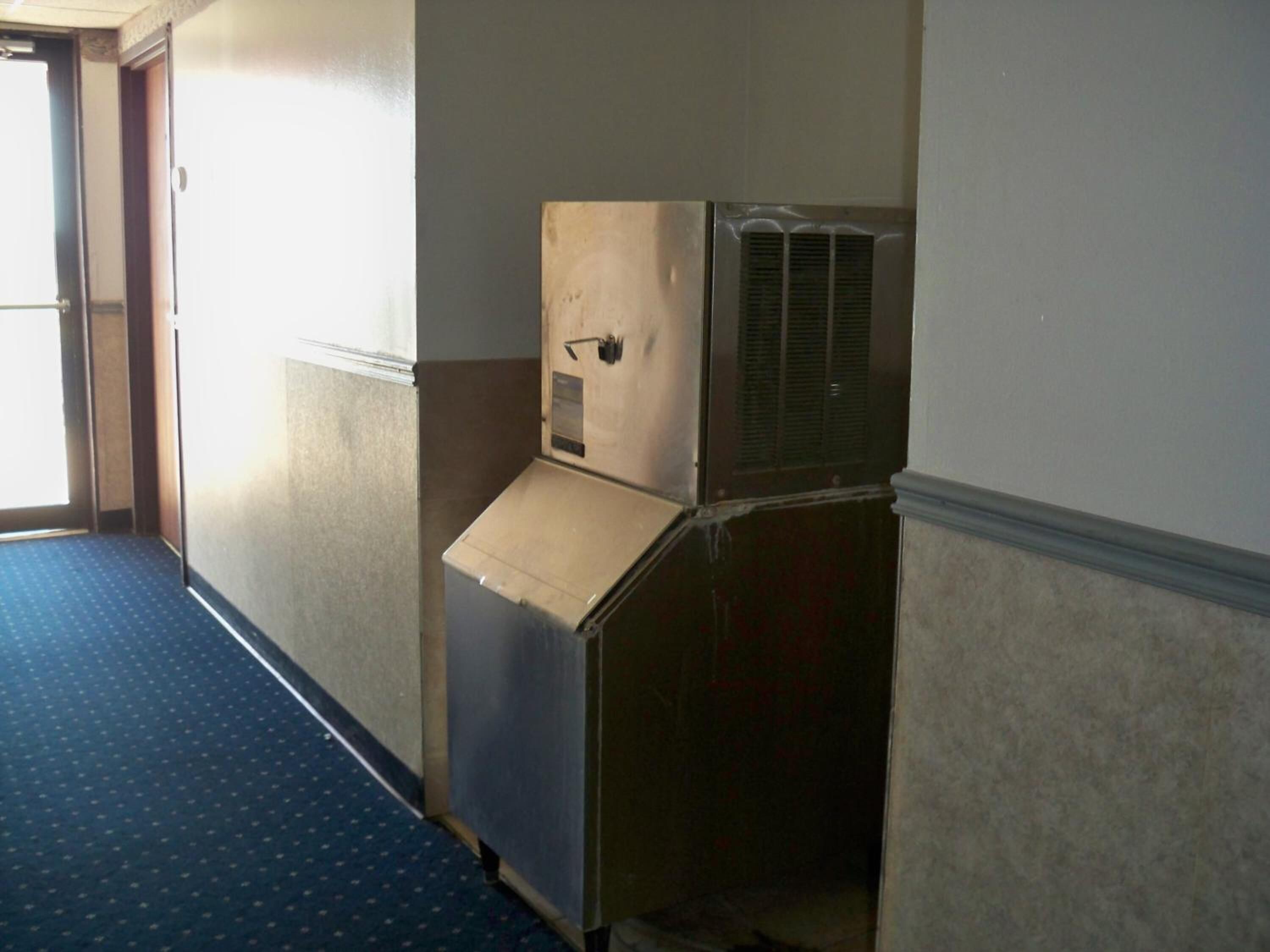 A hallway with a blue carpet, a door, and a wall-mounted air conditioning unit.