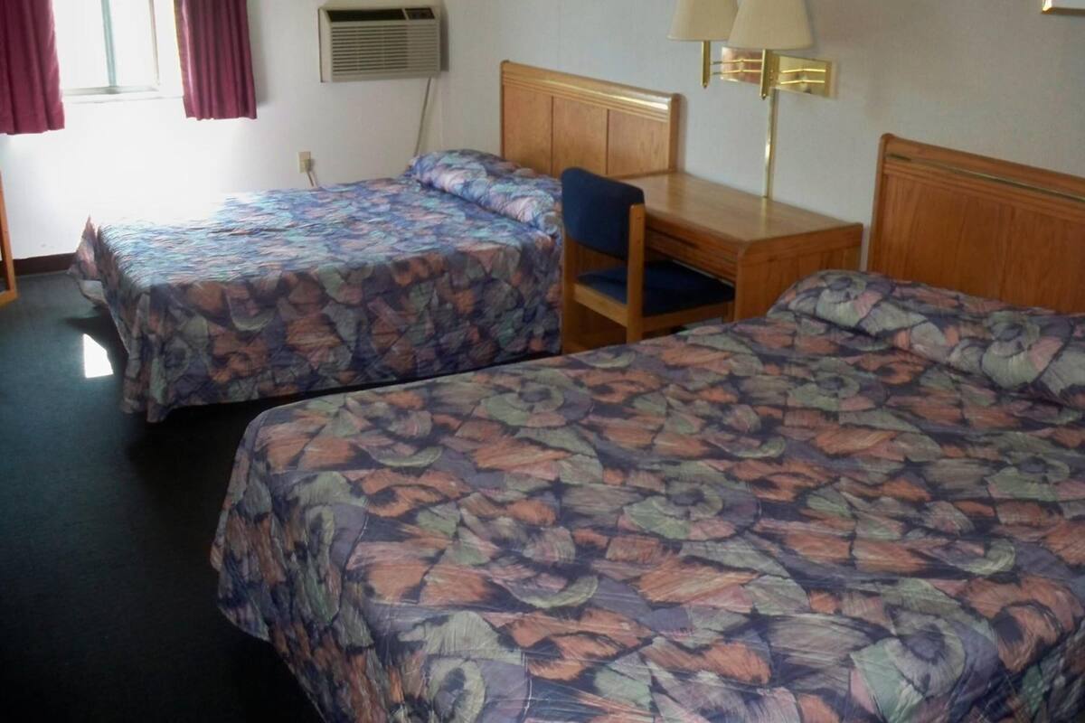 Une chambre d’hôtel avec deux lits, un bureau, une chaise, un appareil de climatisation et une lampe.