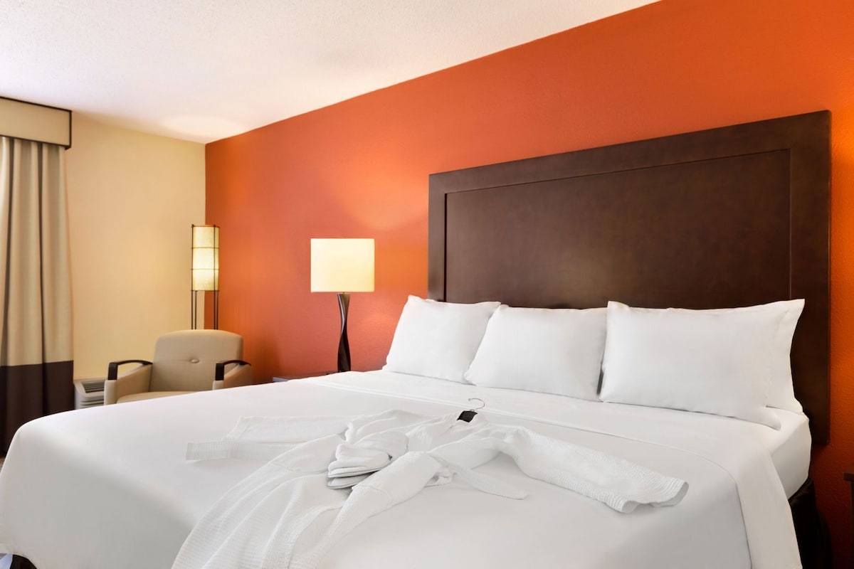 Une chambre d’hôtel avec un grand lit, une chaise, une lampe et une table de chevet.