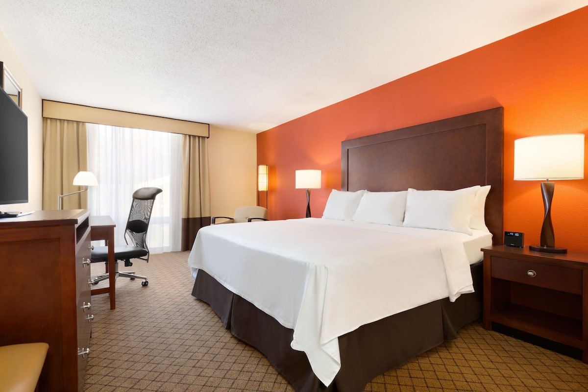 A hotel room with a large bed, a desk with a chair, a TV, and two bedside lamps.