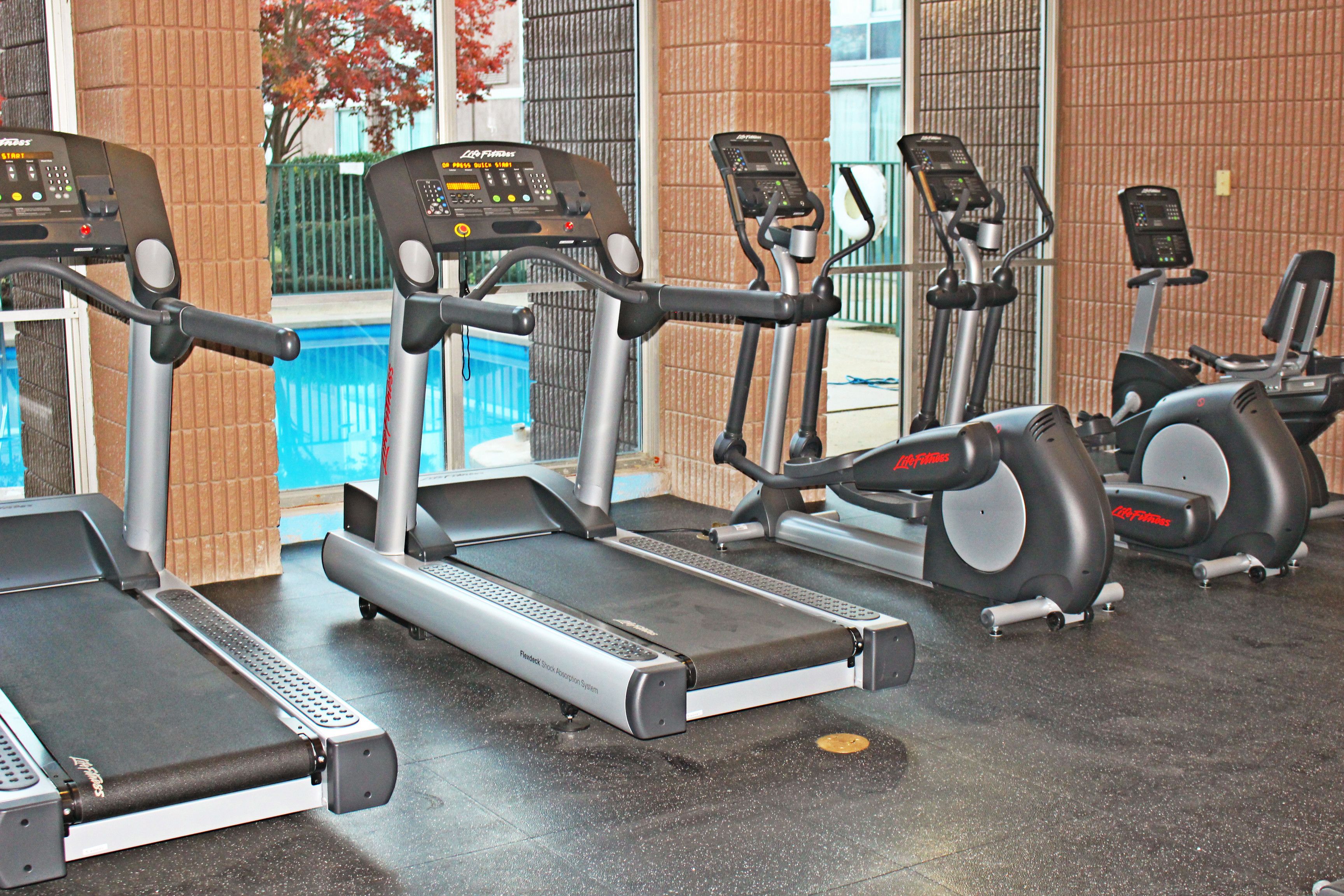 A gym with treadmills, ellipticals, and a pool visible through the window.