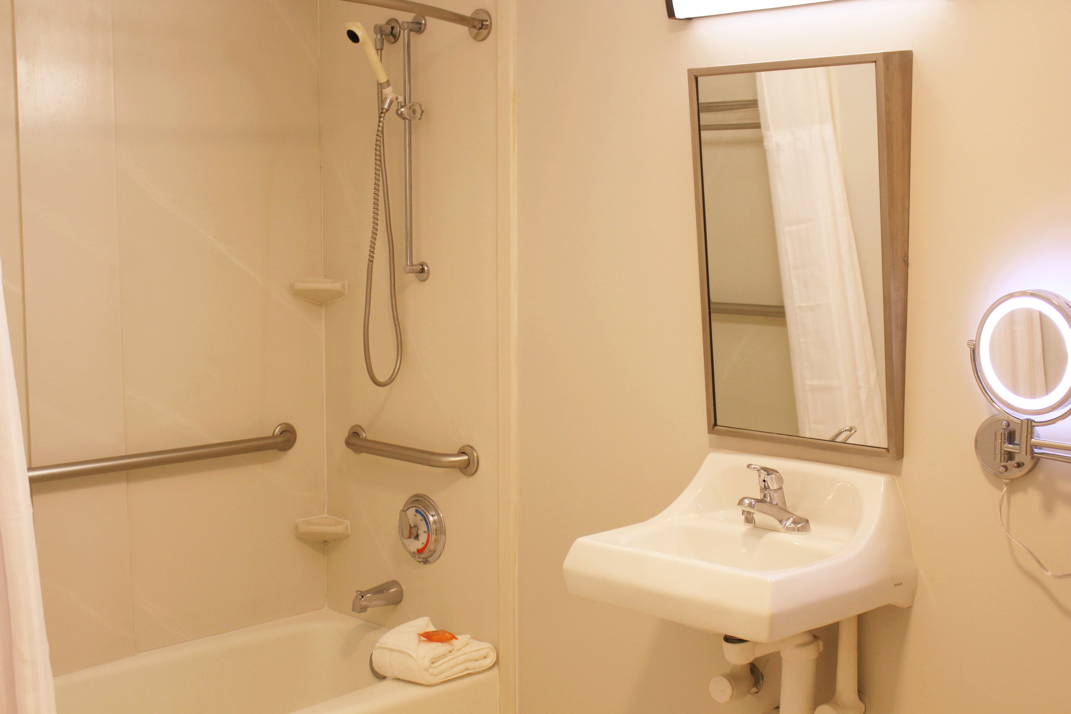 Un baño con bañera, lavamanos, espejo y ducha con barras de apoyo.