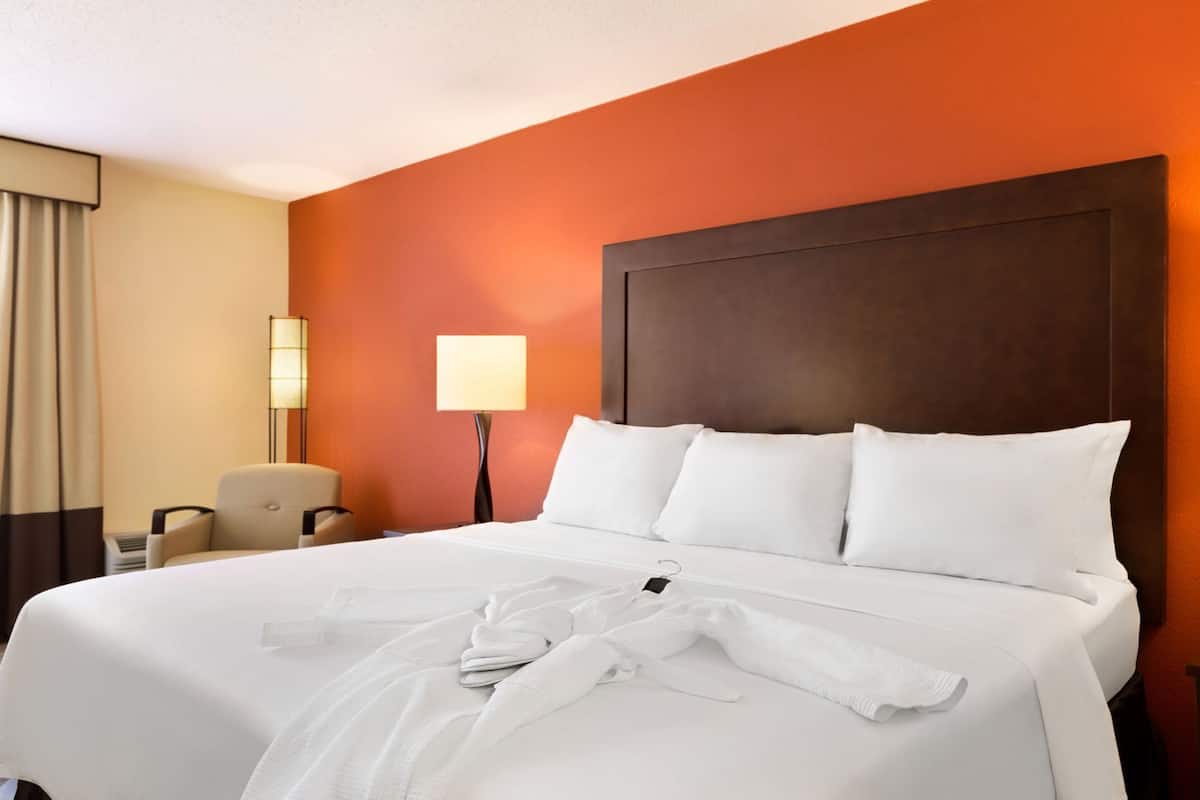 A hotel room with a large bed, a chair, a lamp, and a nightstand.