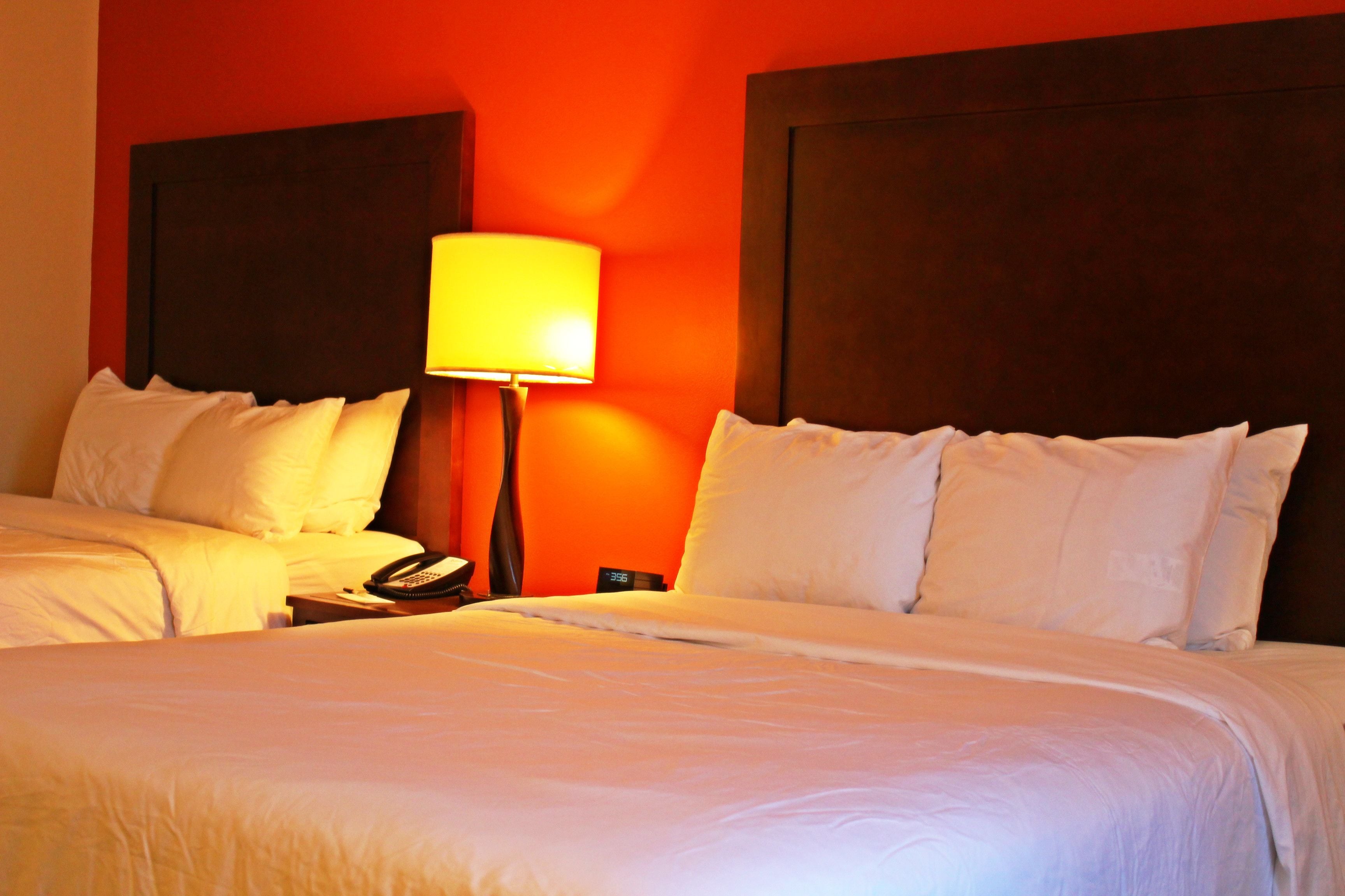 A hotel room with two beds, a nightstand with a lamp, and a telephone.