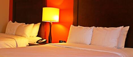 A hotel room with two beds, a nightstand with a lamp, and a telephone.