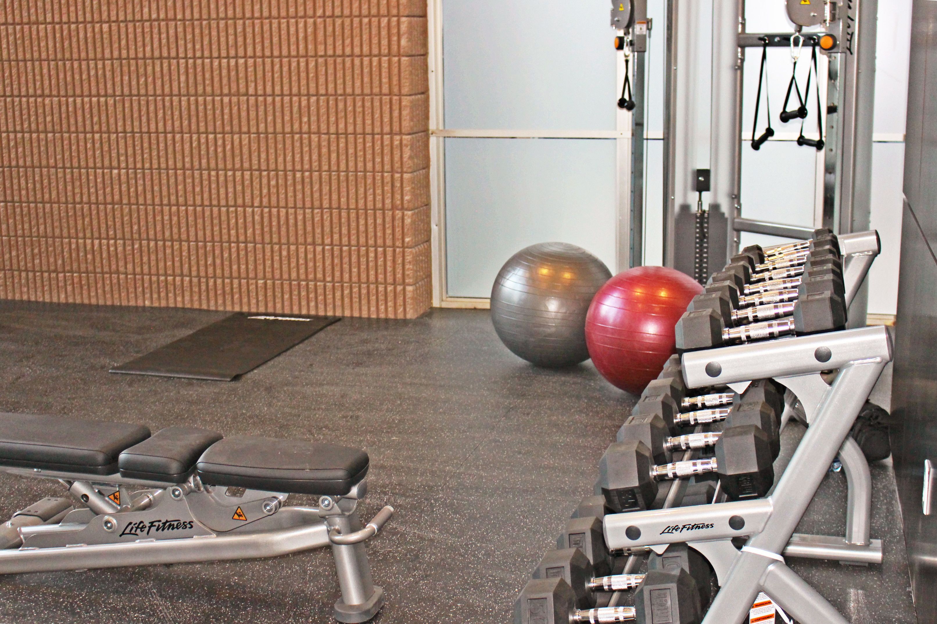 Une salle de sport équipée de matériel de musculation, d’un banc et de ballons d’exercice.