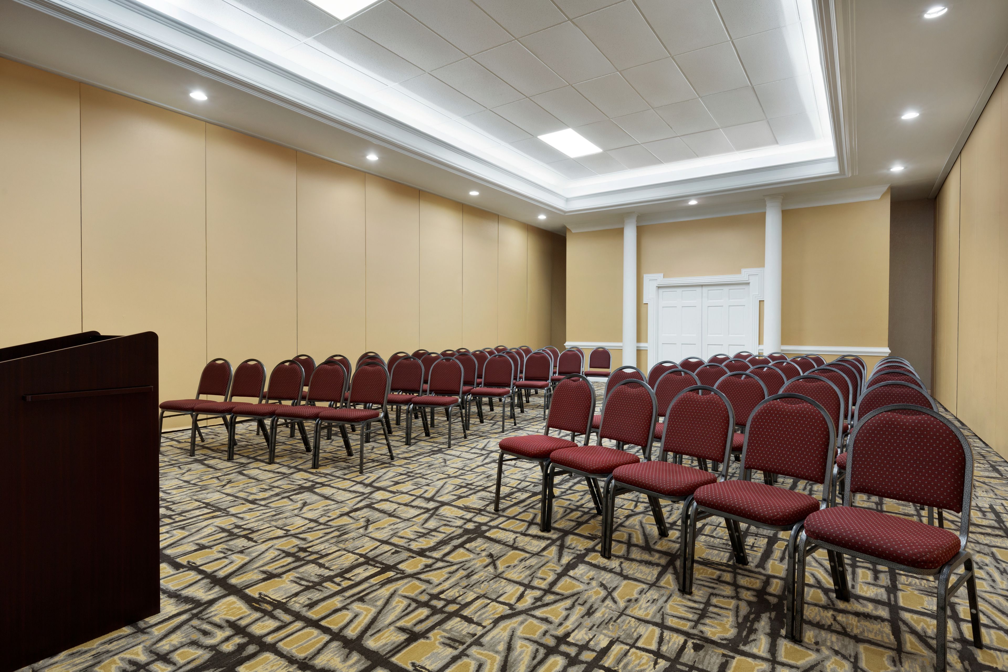 Un salón de conferencias con filas de sillas rojas, un atril y una alfombra estampada.