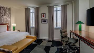 A hotel room with a bed, a desk, a chair, a television, and a window with curtains.