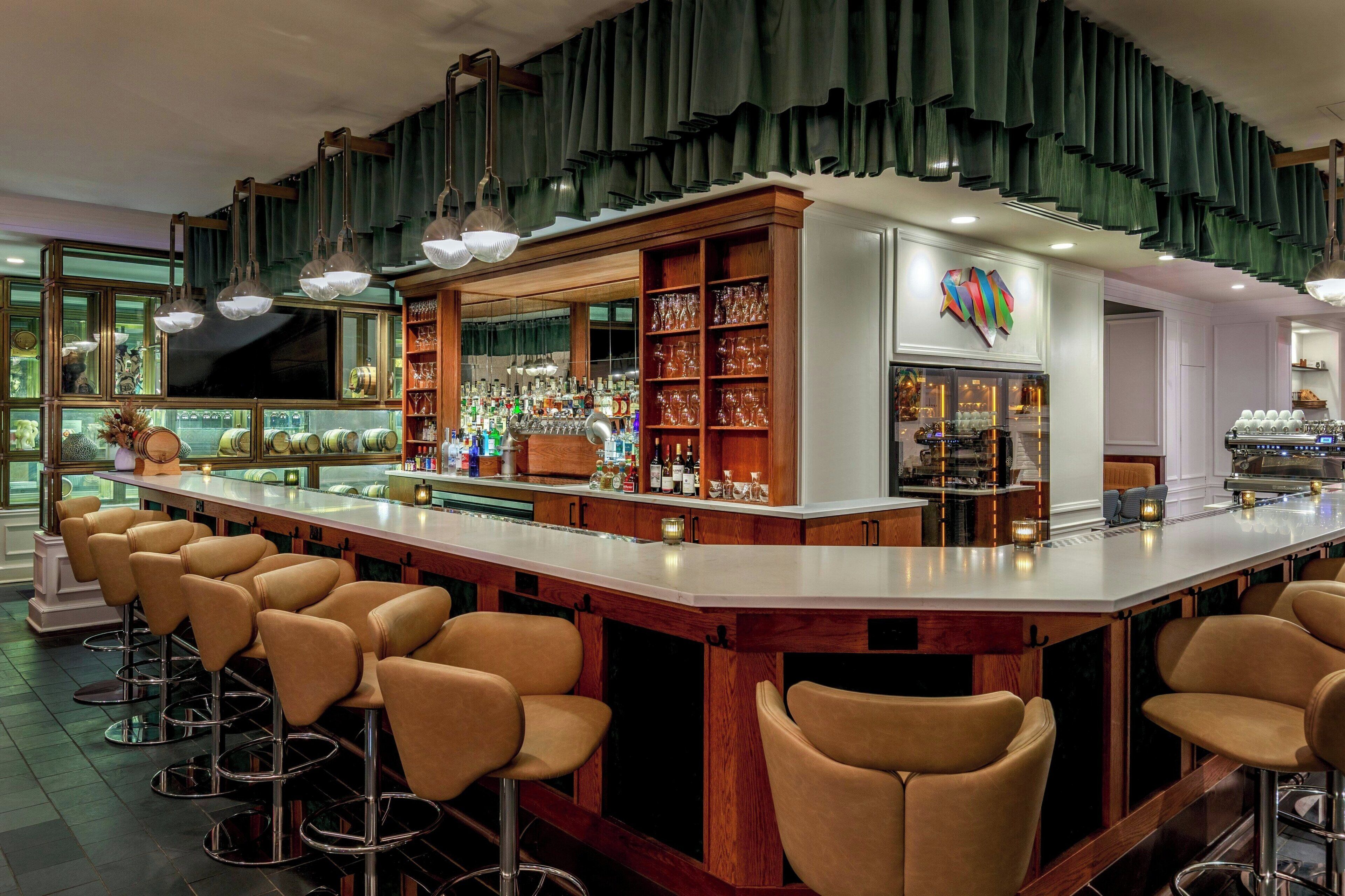 A bar area with a long counter, multiple stools, and a variety of bottles and glasses.