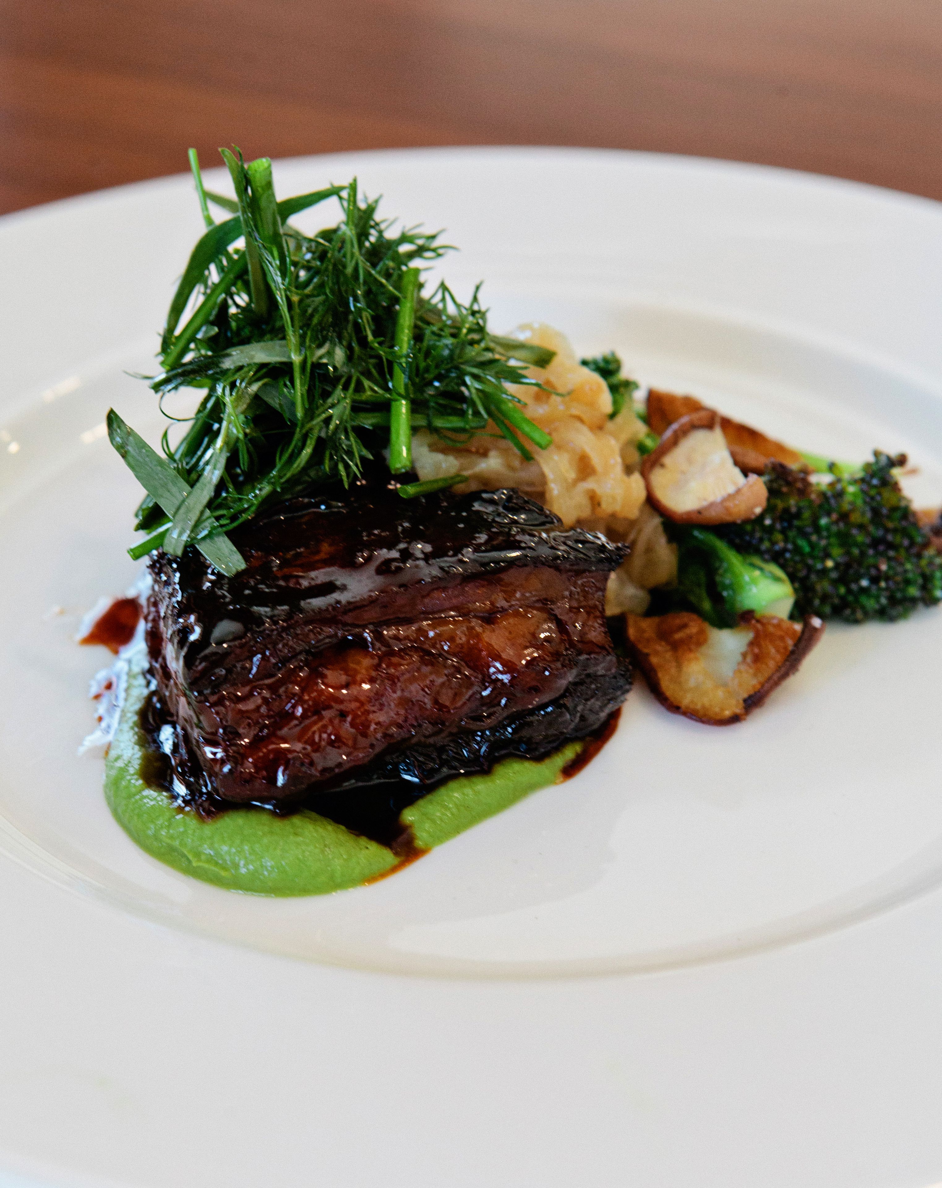 A plate of food with a steak, green vegetables, and a garnish.