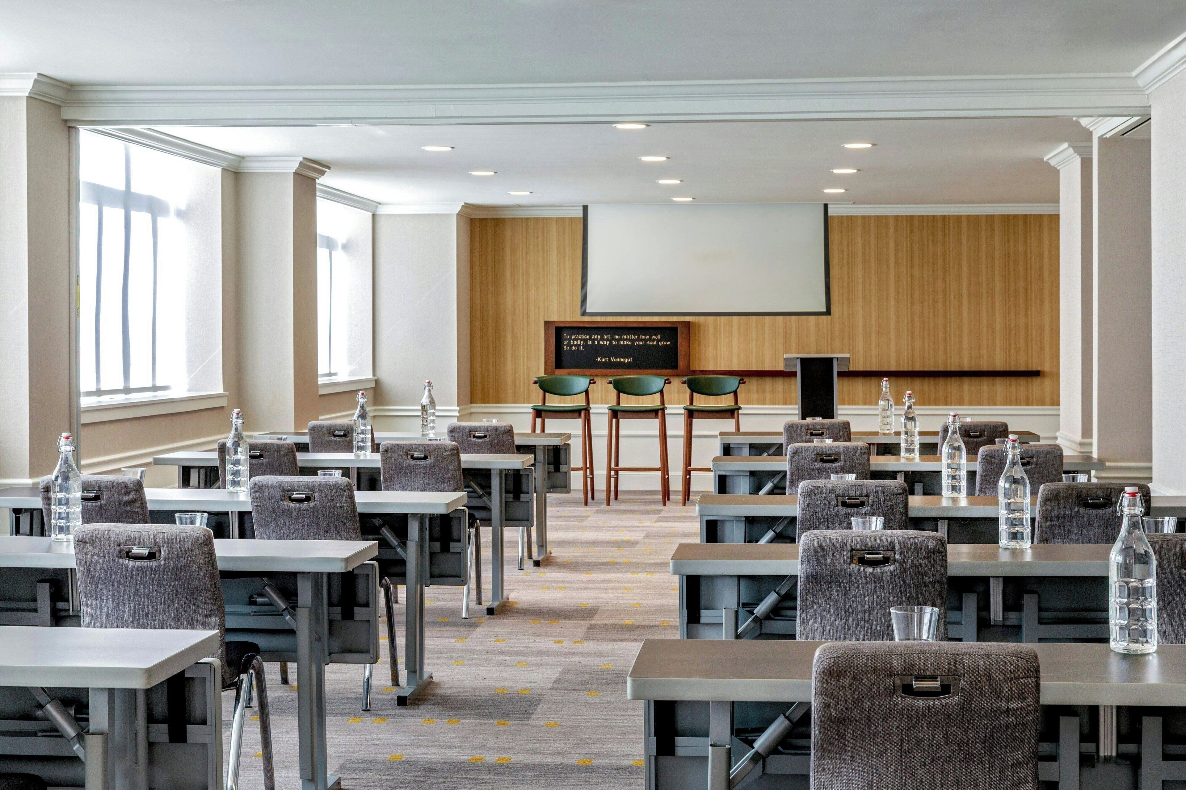 A conference room with tables, chairs, a projector screen, and a podium.