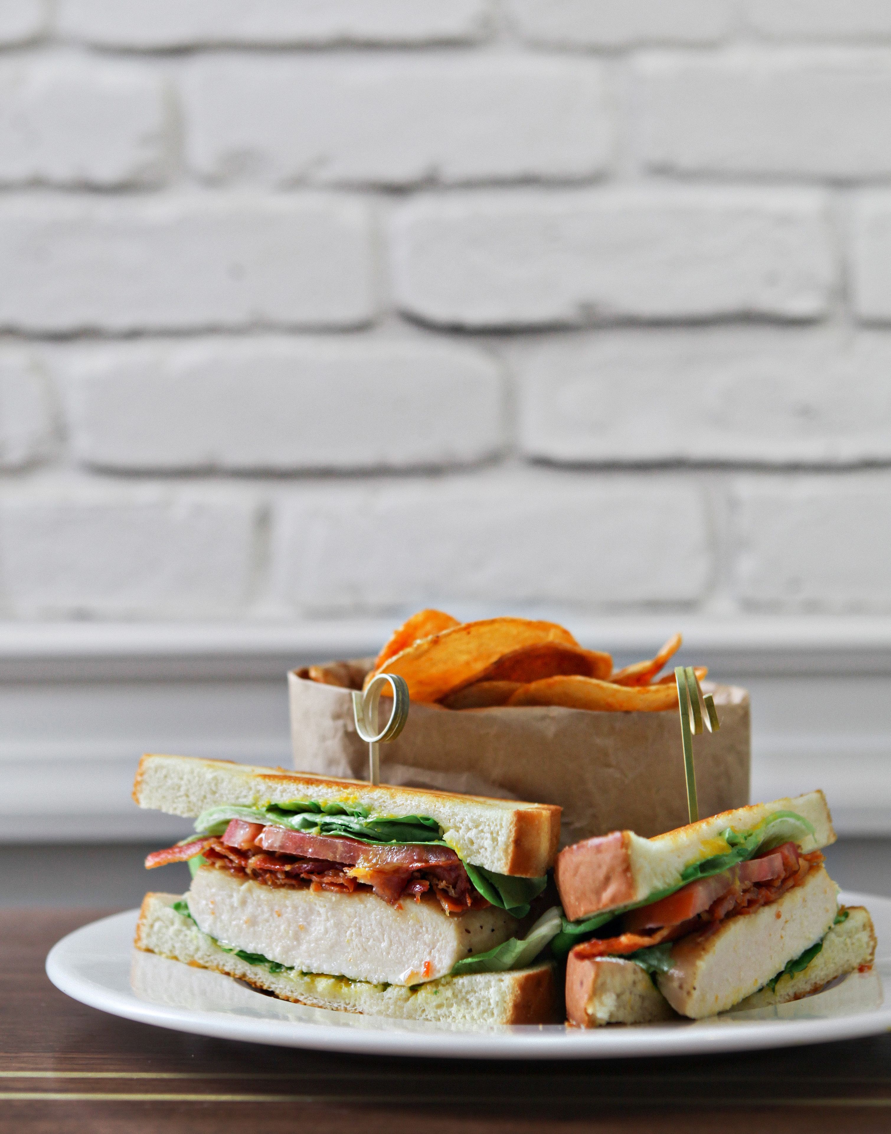 Un sandwich sur une assiette, avec un mur de briques blanches en arrière-plan.