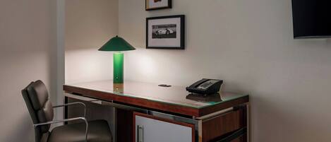 A small office space with a desk, chair, lamp, phone, and framed pictures on the wall.