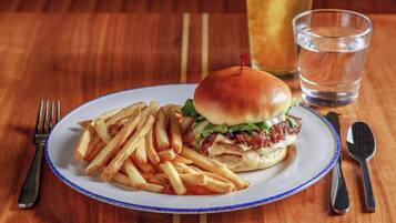 A plate with a burger and fries, a glass of beer, and cutlery on a wooden table.