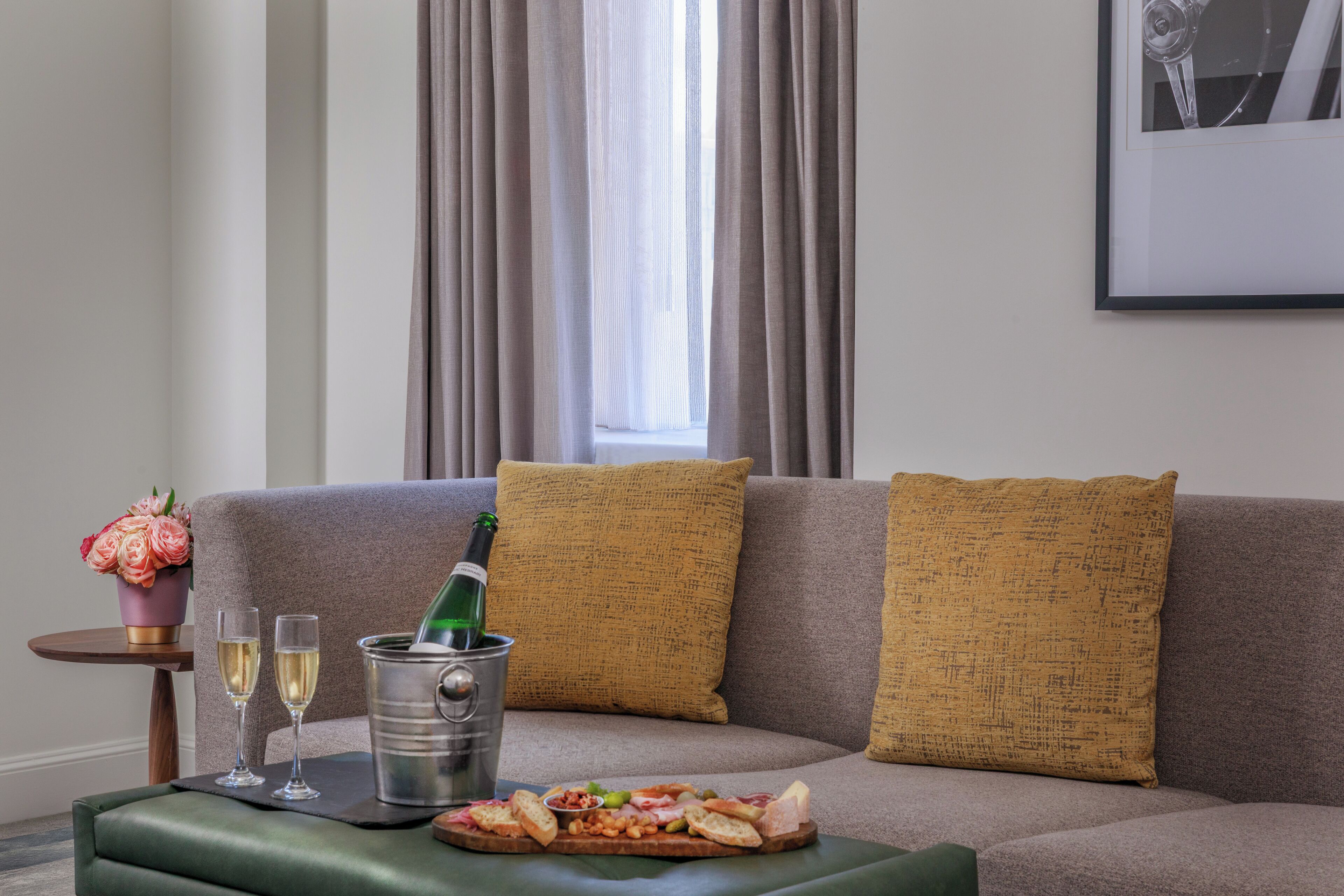 A living room with a sofa, a small table with a bottle of champagne, two glasses, and a tray of snacks.