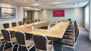 Une salle de conférence avec une longue table, de nombreuses chaises et un grand écran affichant le mot « RÉUNIONS » sur le mur.