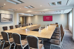 A conference room with a long table, multiple chairs, and a large screen displaying "MEETINGS" on the wall.