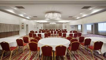 Une grande salle de conférence avec des tables rondes et des chaises rouges, un lustre et un sol recouvert de moquette.