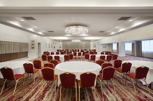 A large conference room with round tables and red chairs, a chandelier, and a carpeted floor.