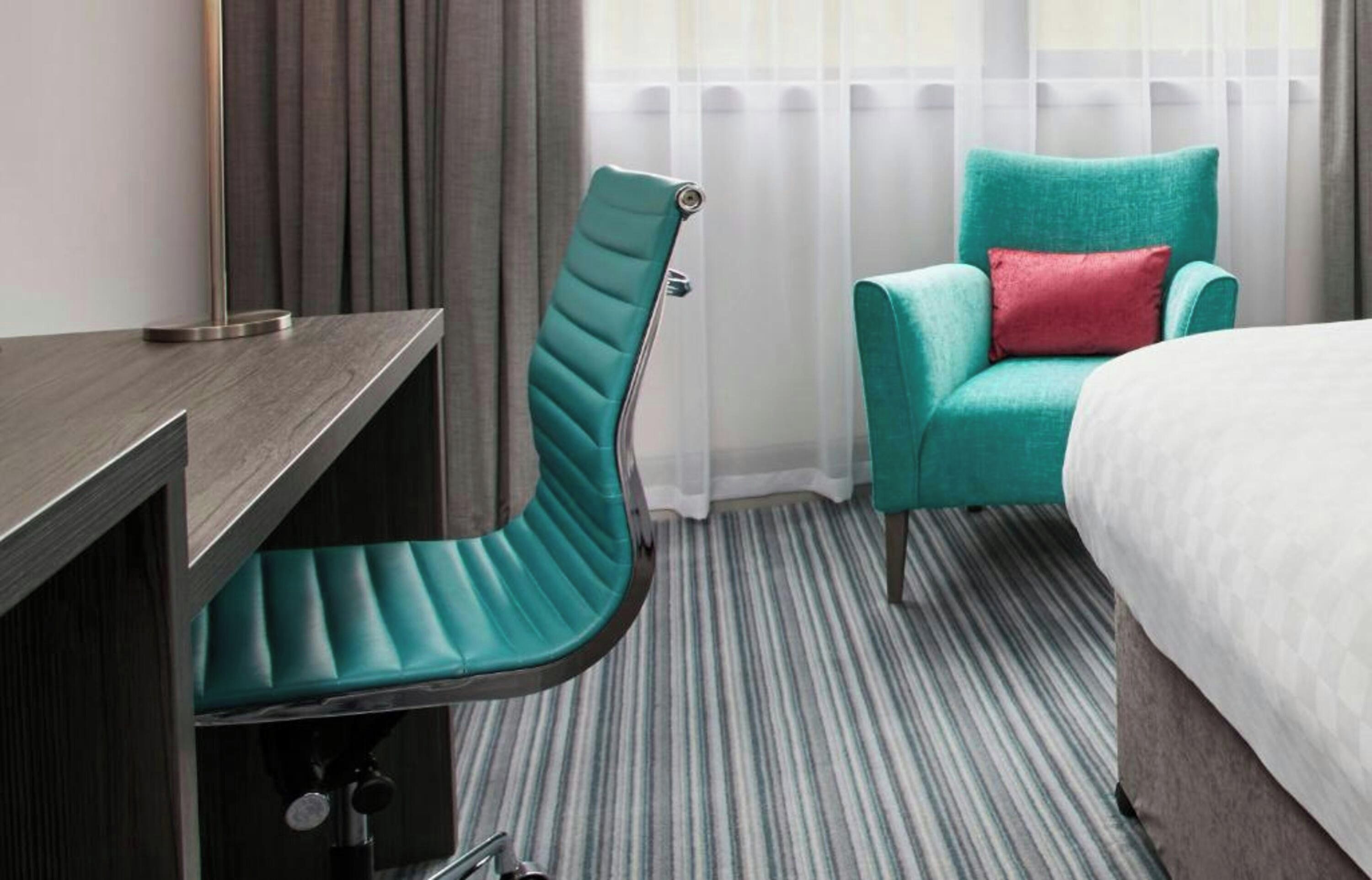 A hotel room with a bed, a desk, a chair, and a window with curtains.