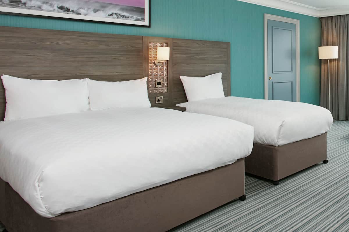 A hotel room with two beds, a headboard with a light fixture, a door, and a framed picture on the wall.