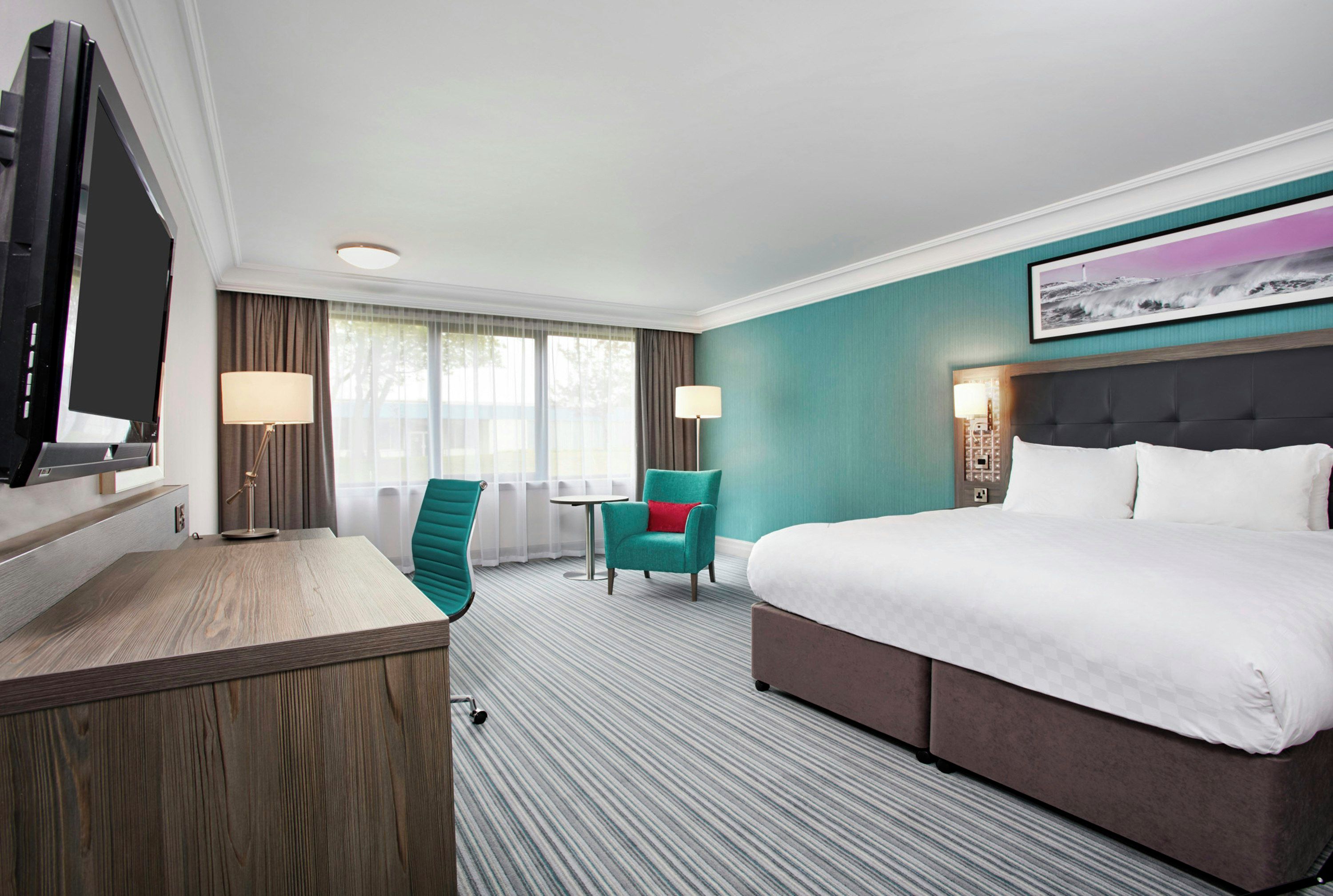 Une chambre d’hôtel équipée d’un lit, d’un bureau, d’une chaise, d’une petite table et d’un téléviseur.