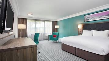 A hotel room with a bed, a desk, a chair, a small table, and a TV.