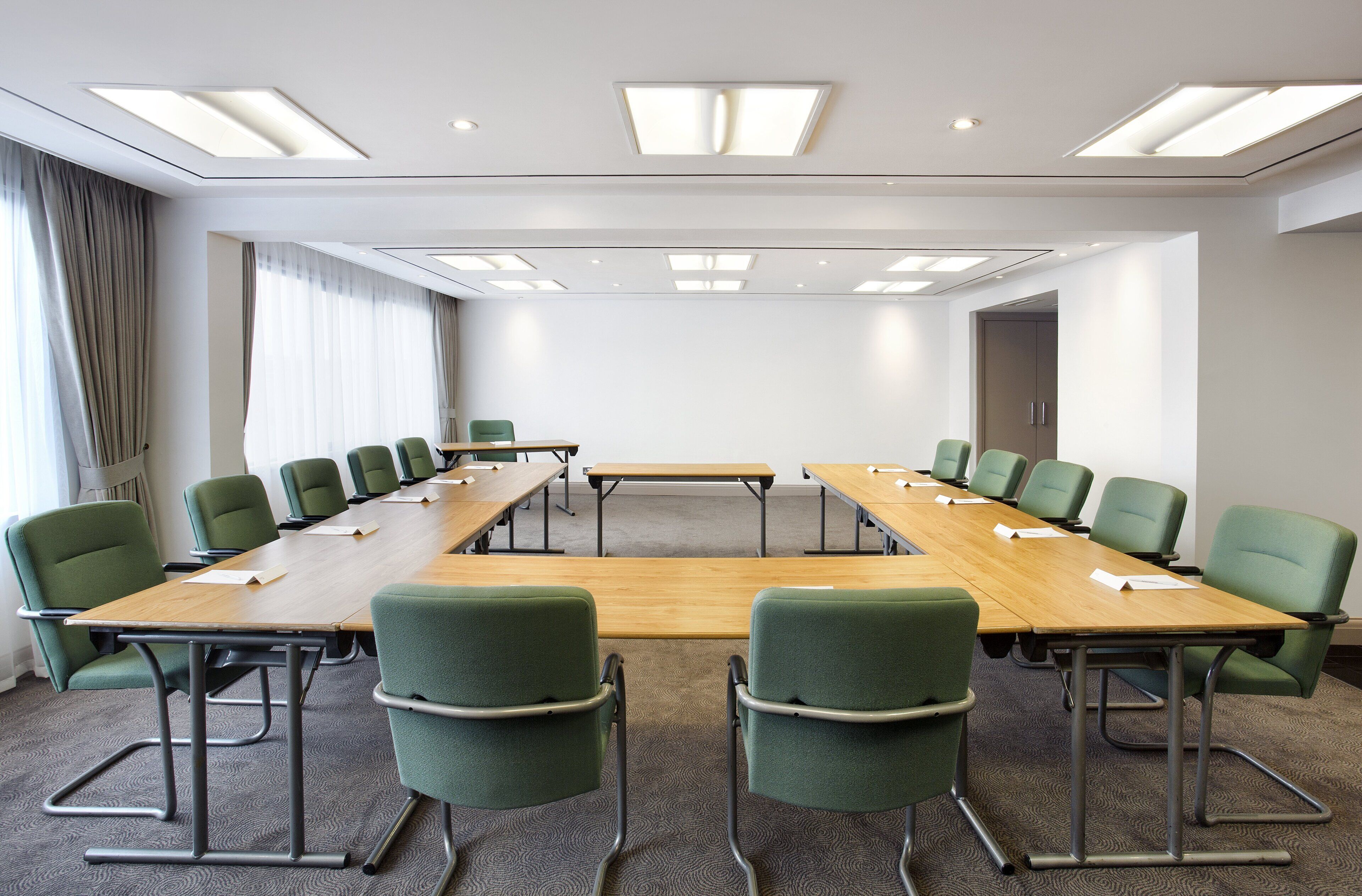 A conference room with a long table, green chairs, and a large window with curtains.