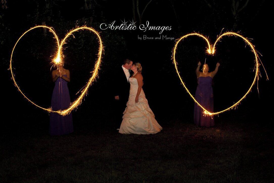 A wedding scene with a bride and two guests holding sparklers forming heart shapes.